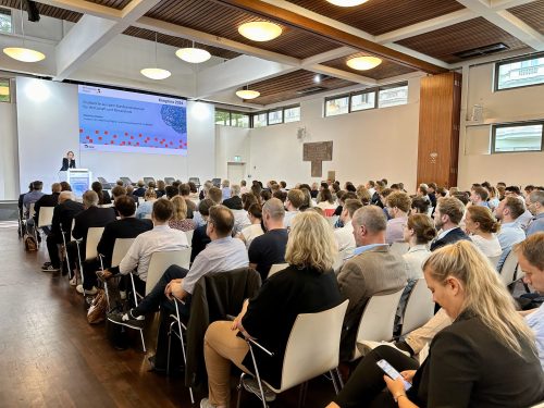 Ein Sall voller Menschen auf Stühlen. Vorn eine Leinwand auf die eine Folie projeziert wird. Christina Decker, Abteilungsleiterin Digital- und Innovationspolitik im BMWK, spricht.