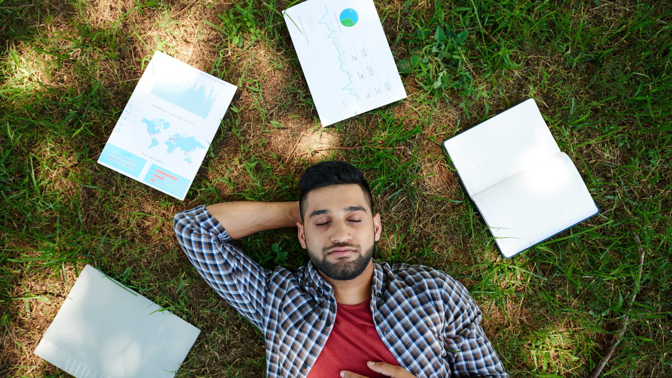 Entlastung Ein Mann liegt entspannt im Gras. Um ihn herum lauter Arbeitsunterlagen