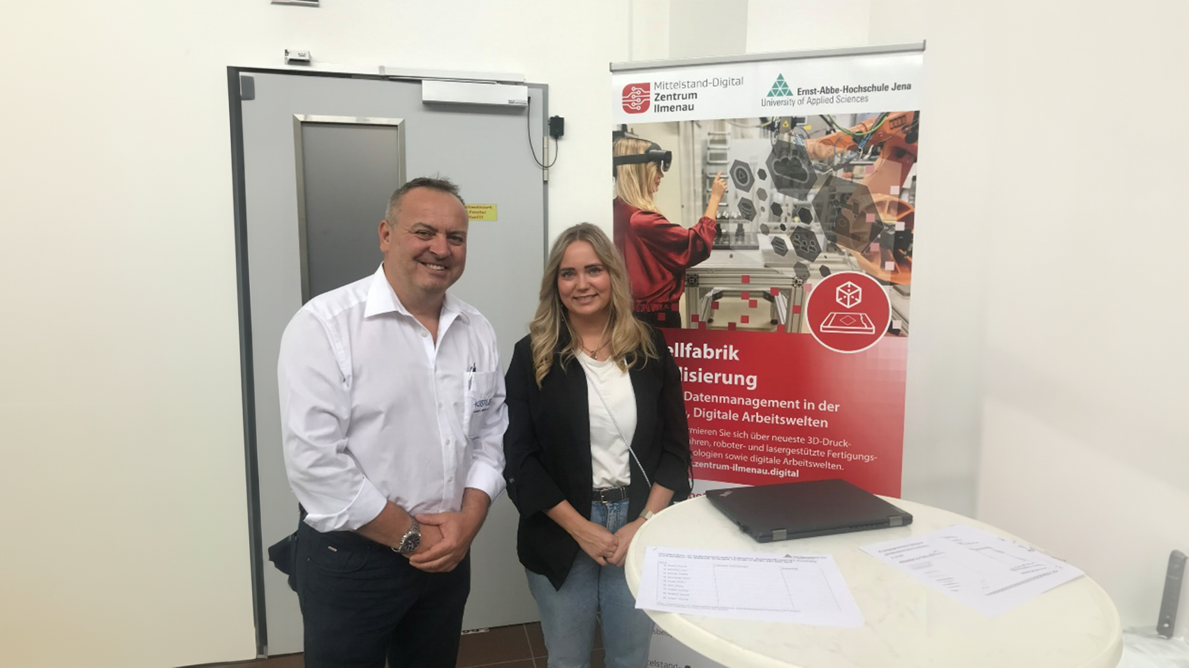 Ein Mann und eine Frau stehen vor einem Banner der Modellfabrik Virtualisierung.