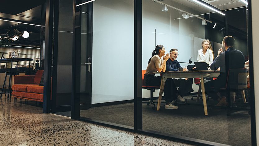 Menschen arbeiten am Tisch Menschen arbeiten an einem Tisch zusammen. Dabei sitzen sie in einem abgetrennten Bereich aus Glas.
