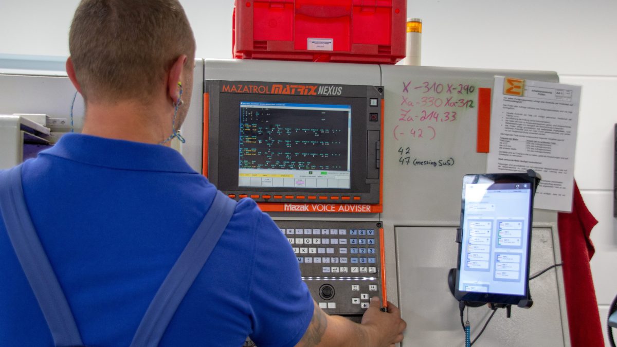 Retrofit im Unternehmen Arbeiter steht vor einer Maschine. An dieser ist ein Tablet befestigt