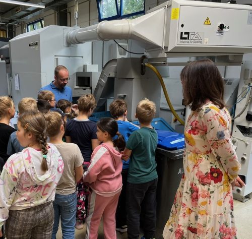 Eine Gruppe von Kindern steht vor einer Maschine in einer Technikhalle