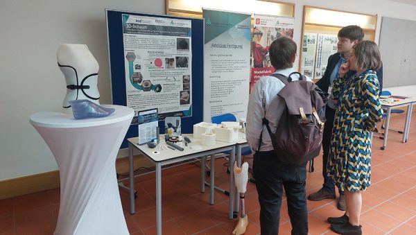 Messestand der Modellfabrik Virtualisierung Menschen vor einem Messestand mit 3D-Druck-Exponaten