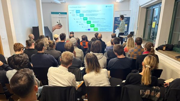 Ein voll besetzter Seminarraum, in dem zahlreiche Personen einem Vortragenden zuhören, der vor einer Projektionsfläche steht und die Entwicklungsphasen eines Startups präsentiert.