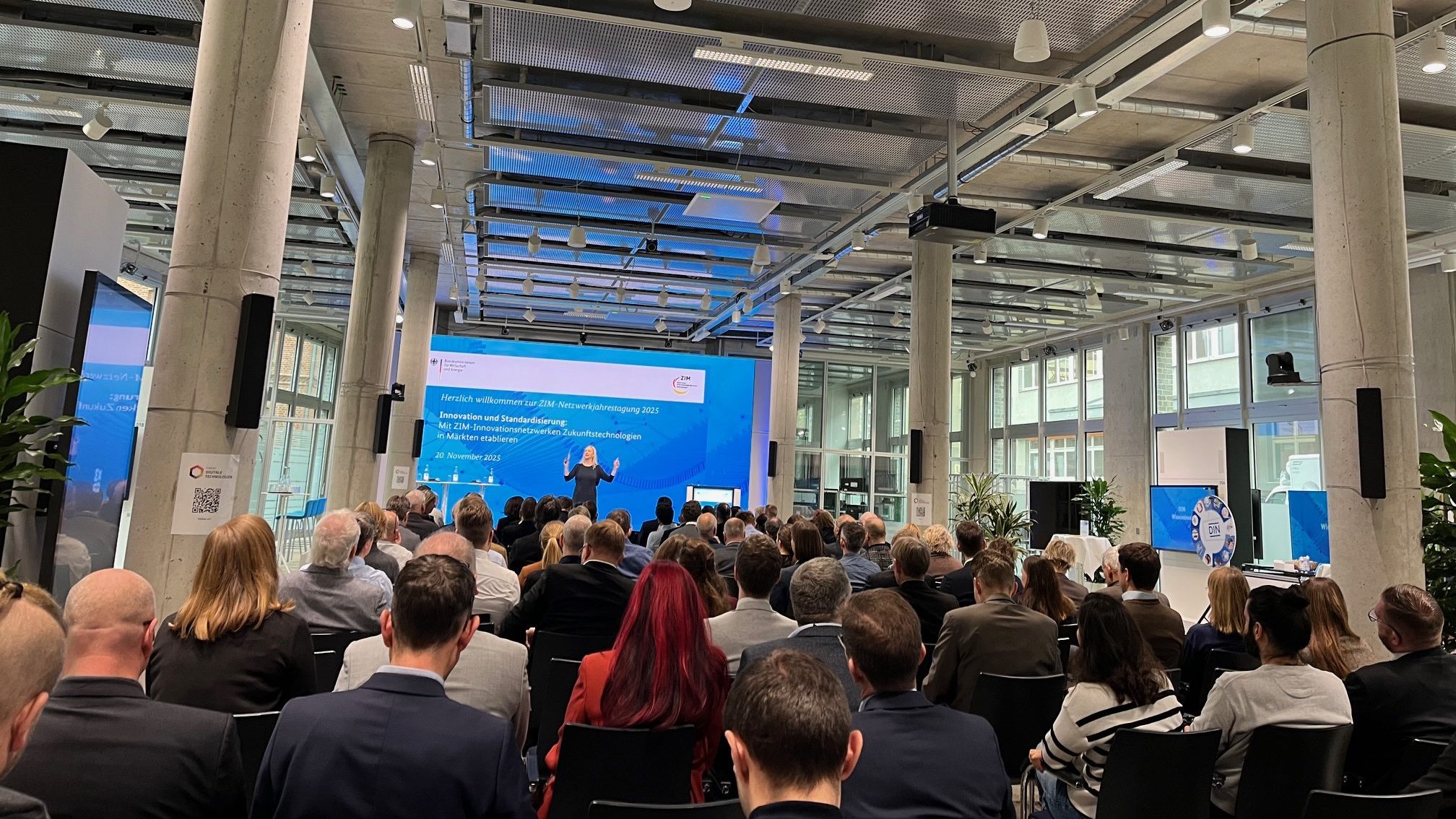 Menschen sitzen in einem Saal und schauen nach vorn auf eine Referentin