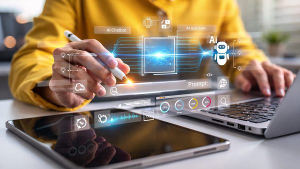 Interaktion mit KI-Anwendungen Person mit gelbem Pullover arbeitet an einem Laptop und Tablet und bedient mit einem weißen Stift eine holografische Benutzeroberfläche mit KI-Elementen und Datenvisualisierungen in einem modernen Büro.