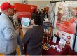 Mehrere Personen stehen an einem Informationsstand des Mittelstand-Digital Zentrums Ilmenau und der Ernst-Abbe-Hochschule Jena. Zu sehen sind Roll-ups zur Modellfabrik Virtualisierung, Informationsmaterialien und ein Demonstrator zum Thema alternatives Investieren mit KI.