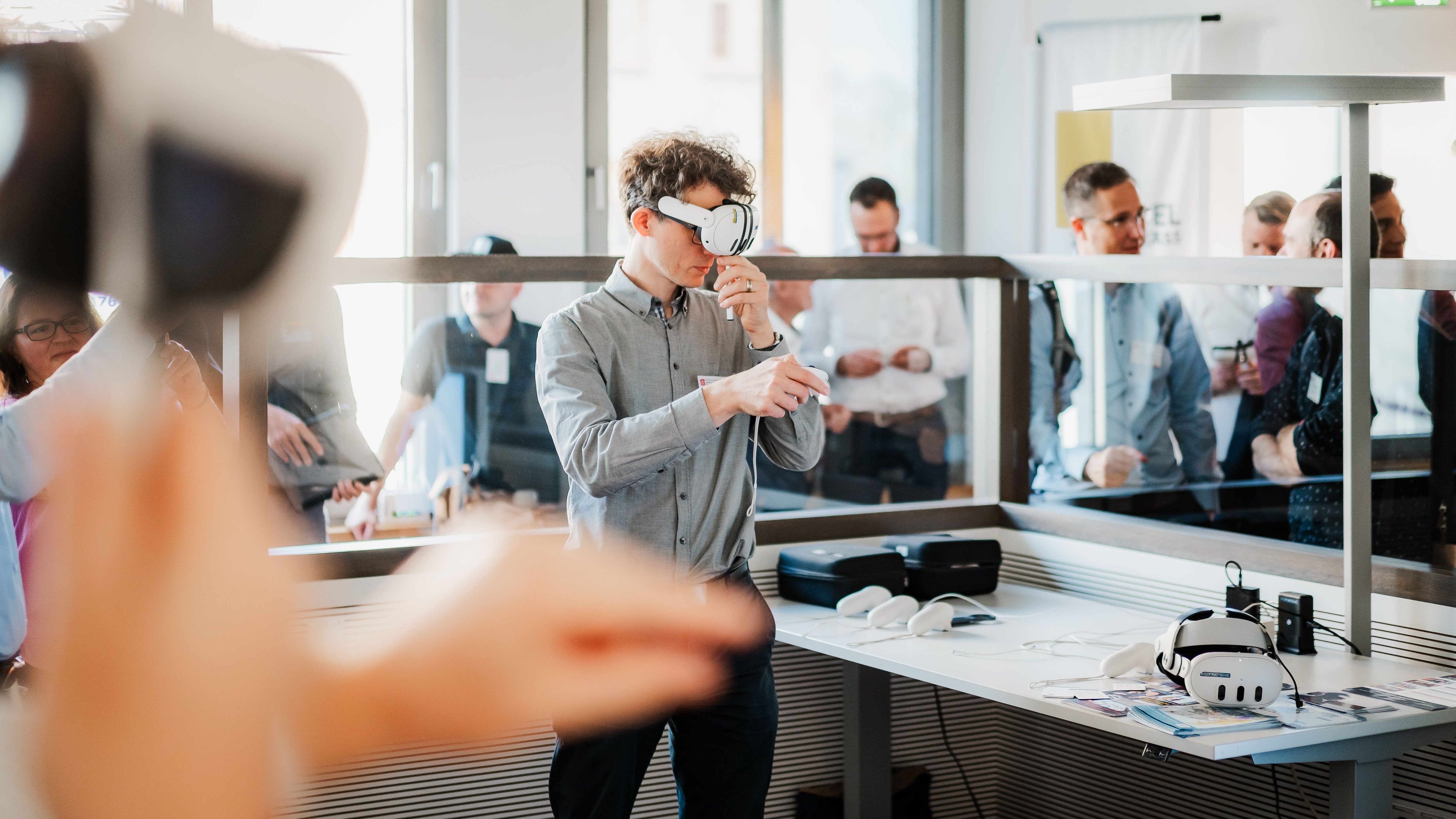 Virtual Reality in der smarten Fertigung Teilnehmer testet eine VR-Brille bei einer Veranstaltung zur smarten Fertigung, während weitere Besucher die Demonstration verfolgen.