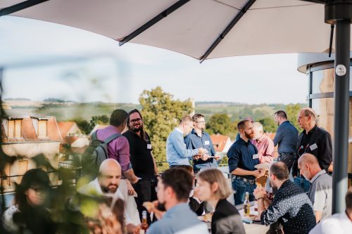 Teilnehmende tauschen sich bei einer Netzwerkveranstaltung auf einer Terrasse aus und führen Gespräche in entspannter Atmosphäre.
