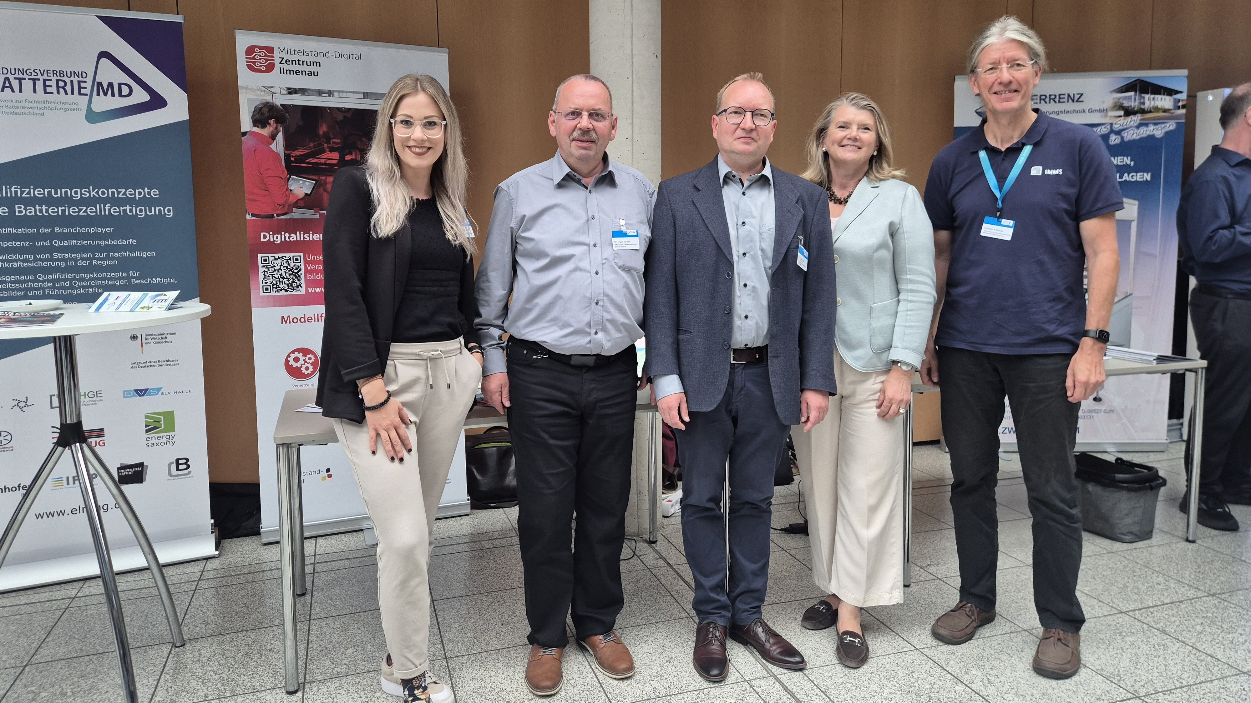 Vertreter:innen beim Mittelstand-Digital Zentrum Ilmenau Fünf Personen stehen gemeinsam vor dem Informationsstand des Mittelstand-Digital Zentrums Ilmenau und weiteren Ausstellungsständen einer Fachveranstaltung.