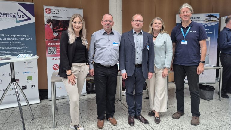 Vertreter:innen beim Mittelstand-Digital Zentrum Ilmenau Fünf Personen stehen gemeinsam vor dem Informationsstand des Mittelstand-Digital Zentrums Ilmenau und weiteren Ausstellungsständen einer Fachveranstaltung.