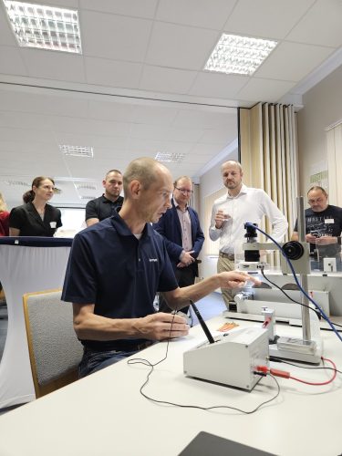 Referent demonstriert an einem Prüf- und Messaufbau die praktische Anwendung der Crimptechnik vor einer Gruppe von Teilnehmenden.