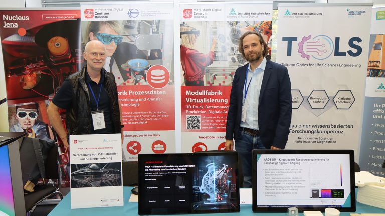 Zwei Aussteller stehen vor Informationsständen zu KI-basierter Visualisierung, Prozessdaten und digitaler Fertigung mit mehreren Monitoren und Demonstrationsmaterialien.