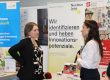 Zwei Teilnehmerinnen im Gespräch vor Informationsständen zu Innovation, Digitalisierung und Technologietransfer.