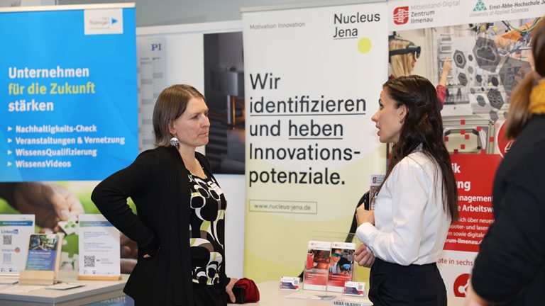 Zwei Teilnehmerinnen im Gespräch vor Informationsständen zu Innovation, Digitalisierung und Technologietransfer.